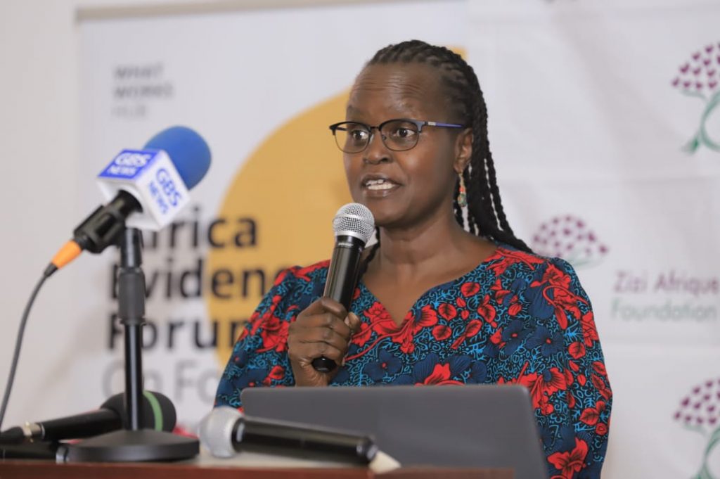 A photo of a woman wearing a blue and red patterned top speaking into a microphone stood behind a podium